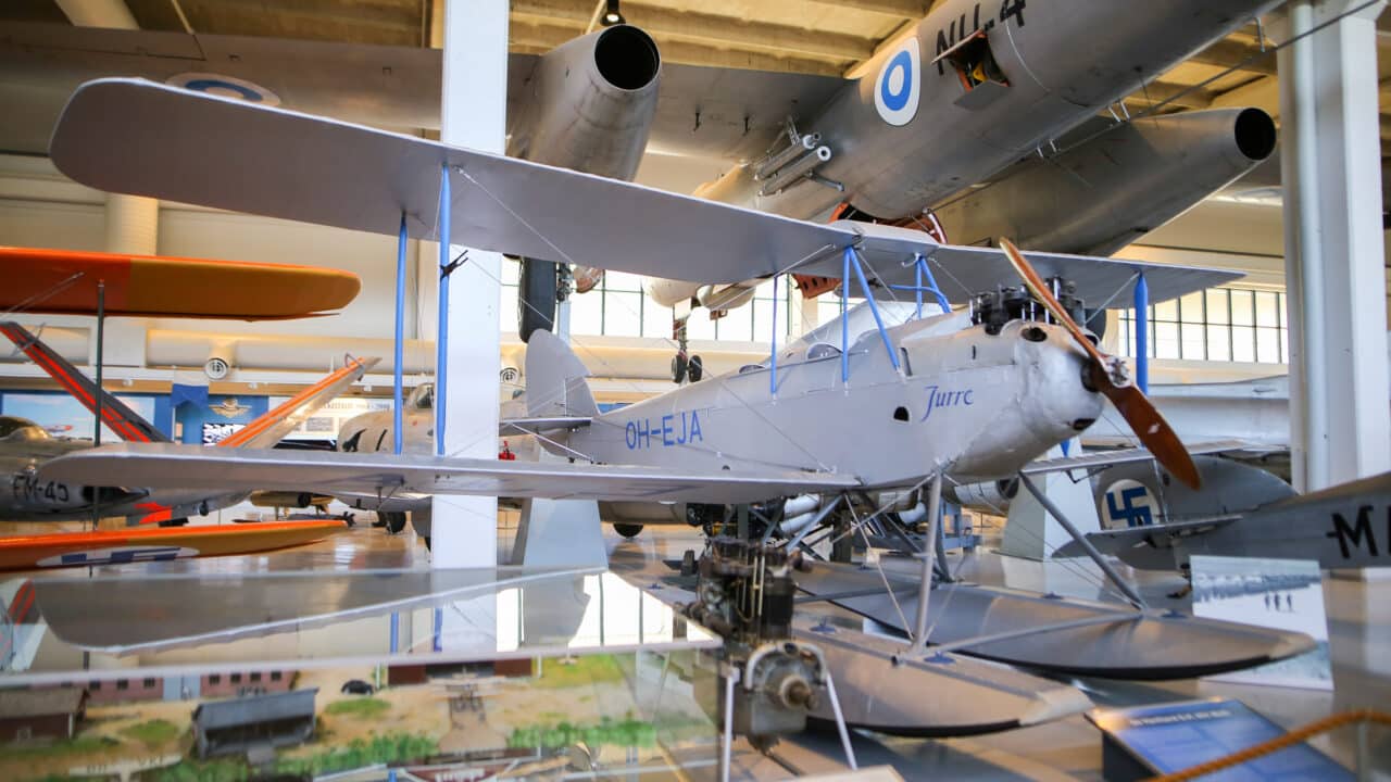 Harmaa, kellukkeilla varustettu Moth-lentokone näyttelyhallissa.