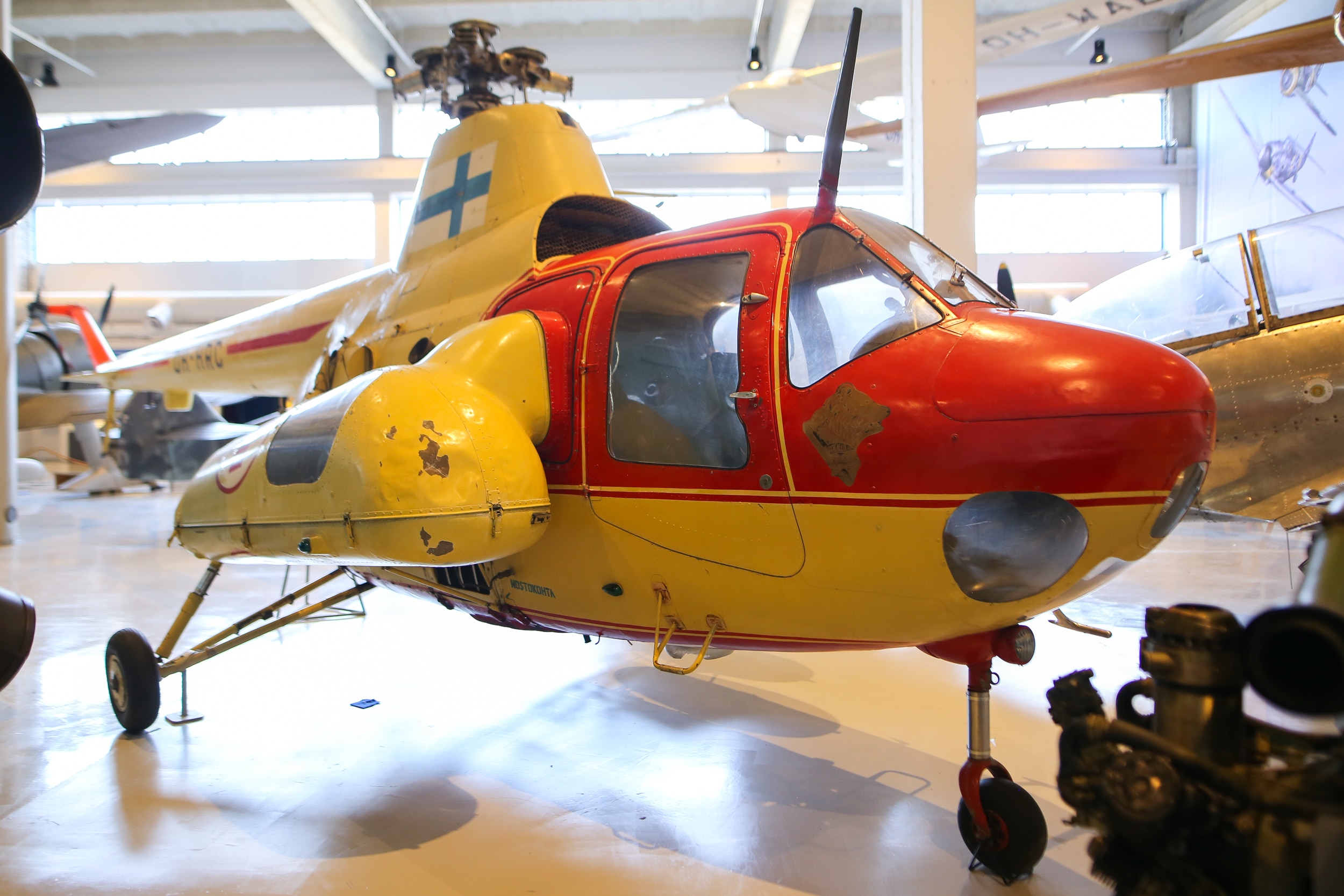 Kelta-punainen helikopteri näyttelyhallissa. Kopterin oikeassa kyljessä on sairaankuljetusta varten konsoli.